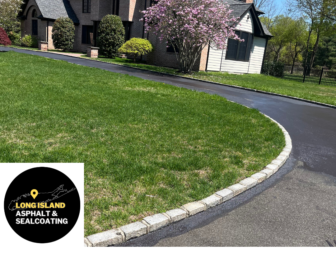 Black asphalt driveway with a stone border next to green grass and a house.