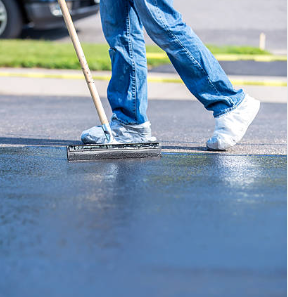 Person in jeans applying sealant to asphalt with a squeegee.