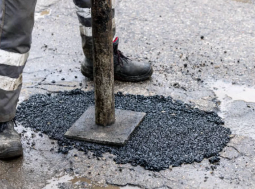 Person compacting asphalt patch on a wet road with a handheld tamper.