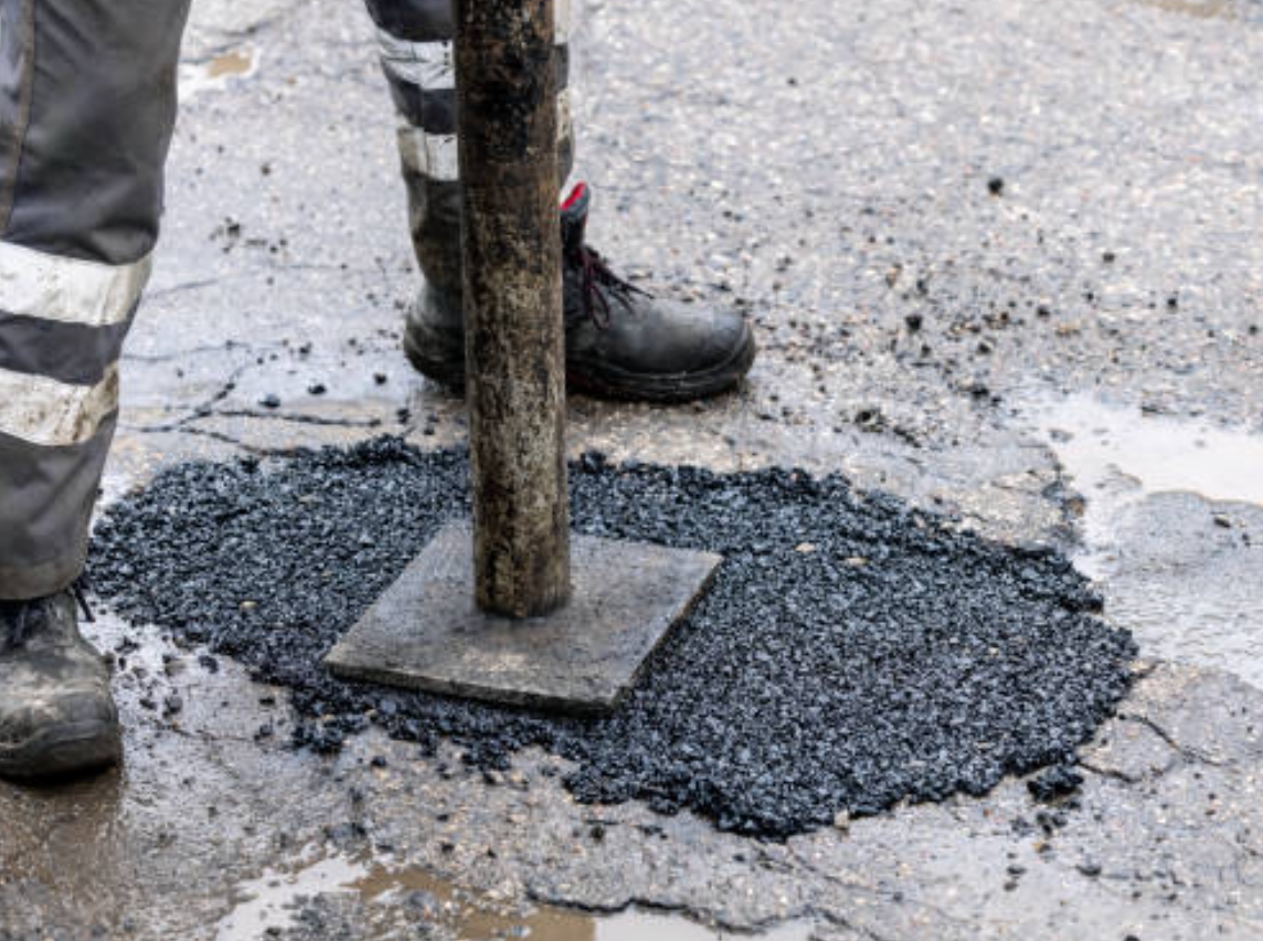 Person patching asphalt with a hand tamper on a wet street.
