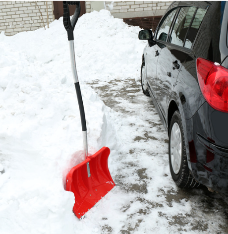 Red snow shovel in deep snow next to a black car parked on a snowy driveway.