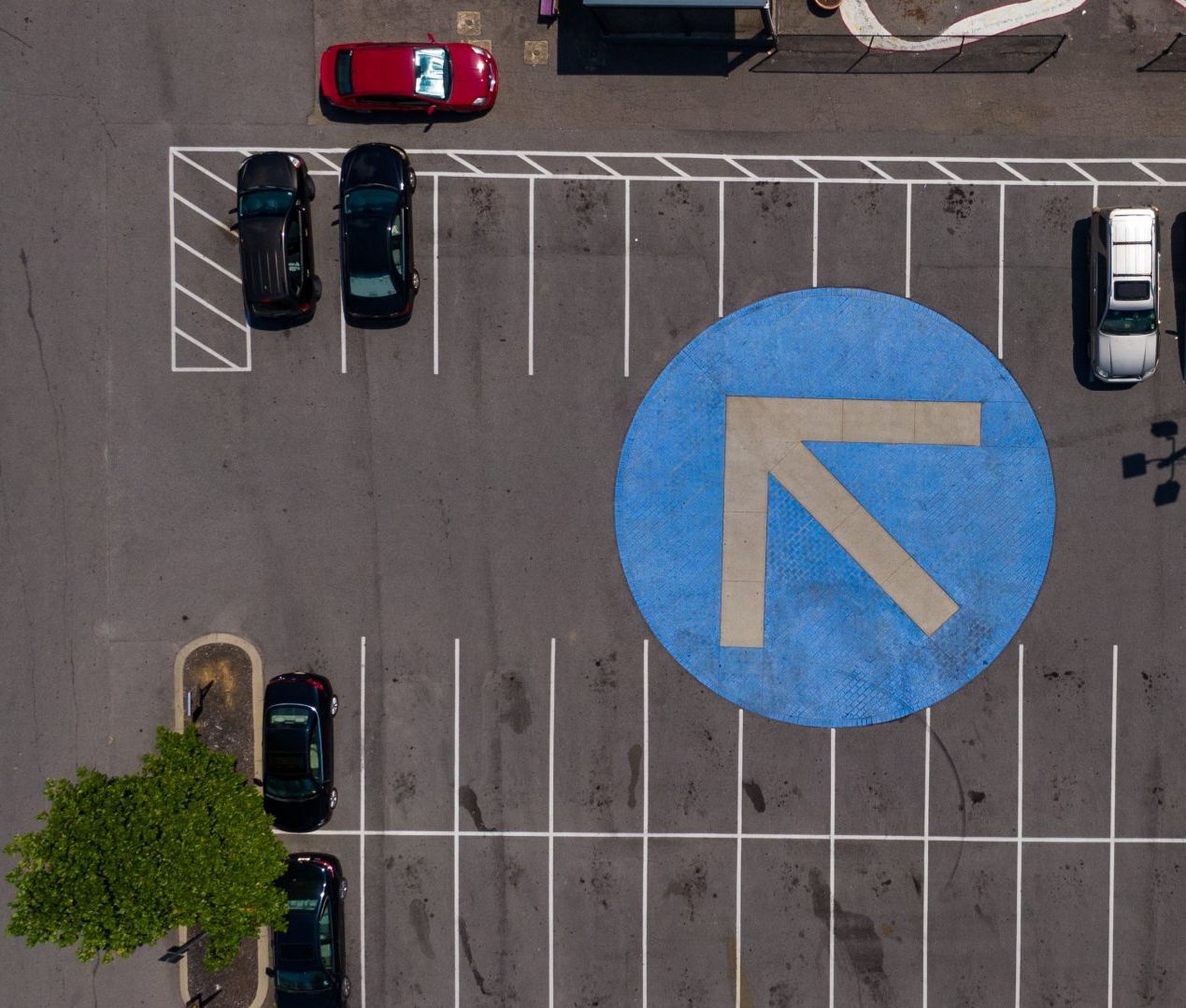 Overhead view of a parking lot with cars parked in stalls, a blue circle with a white arrow.