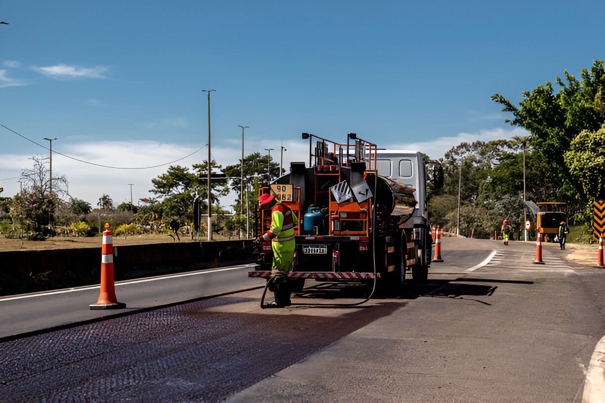 Road paving truck applying asphalt on a sunny day. Orange cones mark the construction zone.