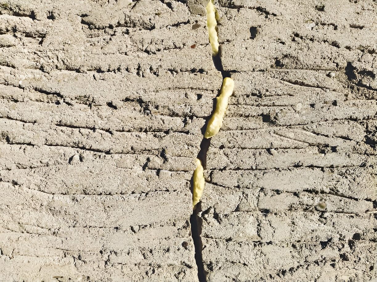 Close-up of a concrete surface with a vertical crack filled with yellow sealant.