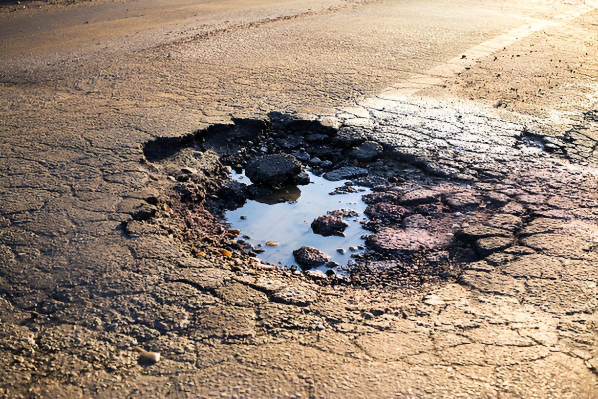 Pothole in asphalt road, filled with water, surrounded by cracks.