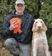 A man is kneeling down next to a dog holding a ribbon.