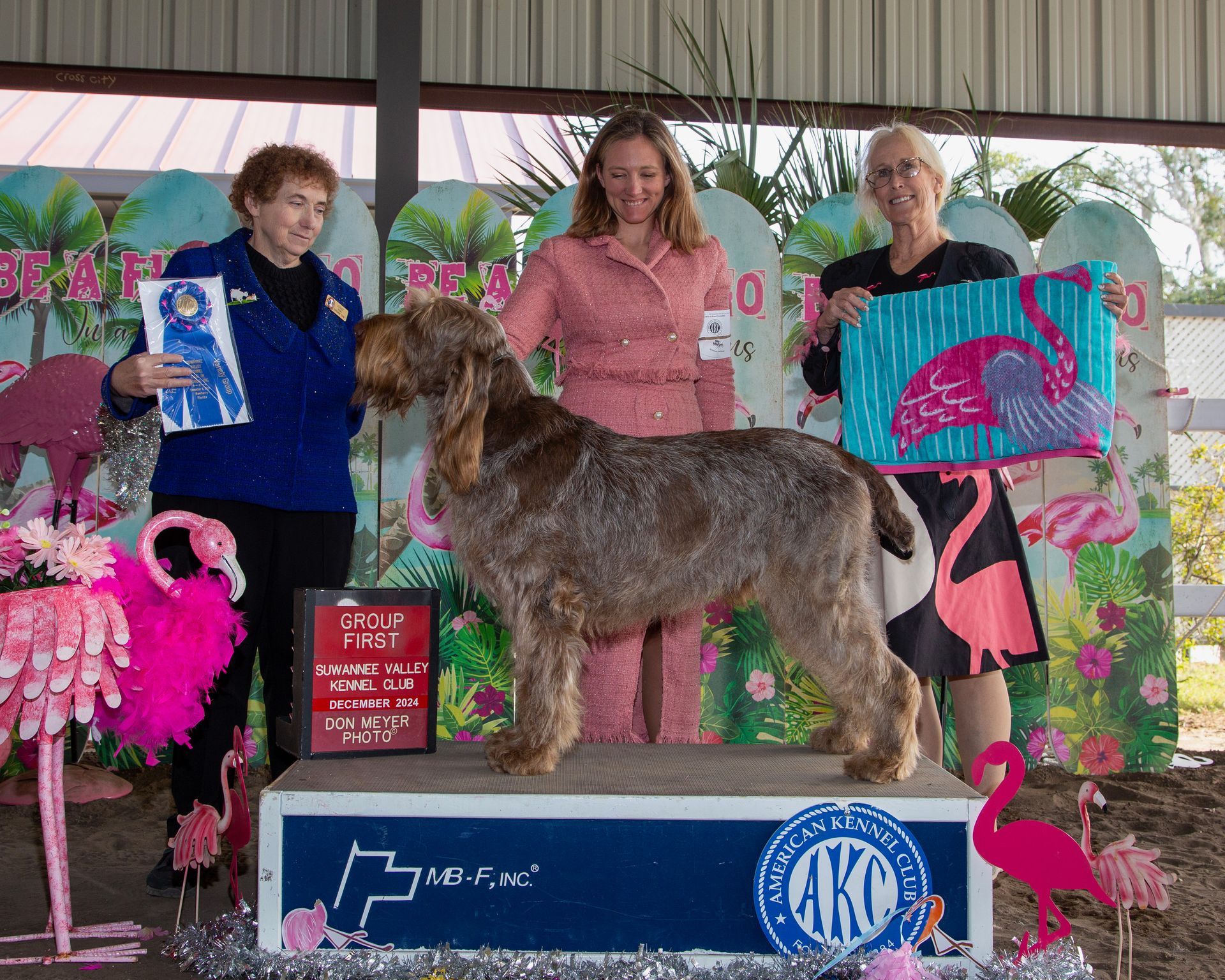 A man is kneeling next to a dog with a ribbon around its neck.