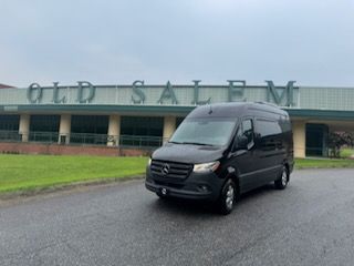 Black van parked on wet pavement in front of the Old Salem building sign.