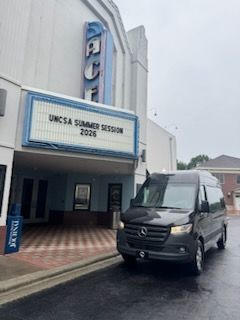Entrance of a building with a sign for “UNCSA SUMMER SESSION 2026” and a black van parked outside