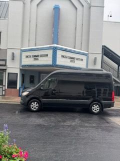 Black van parked in front of a theater entrance with a blue marquee.