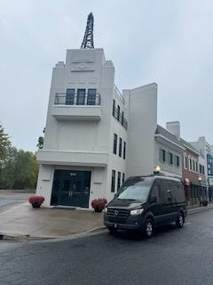 White building with a tall antenna and a black van parked in front on a wet street