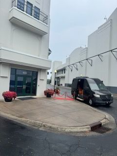 Black van parked by a white building entrance with pink flowers and a curved driveway