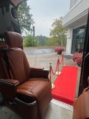 Luxury van interior with brown leather seats, opening to a red carpet walkway outside on a rainy day