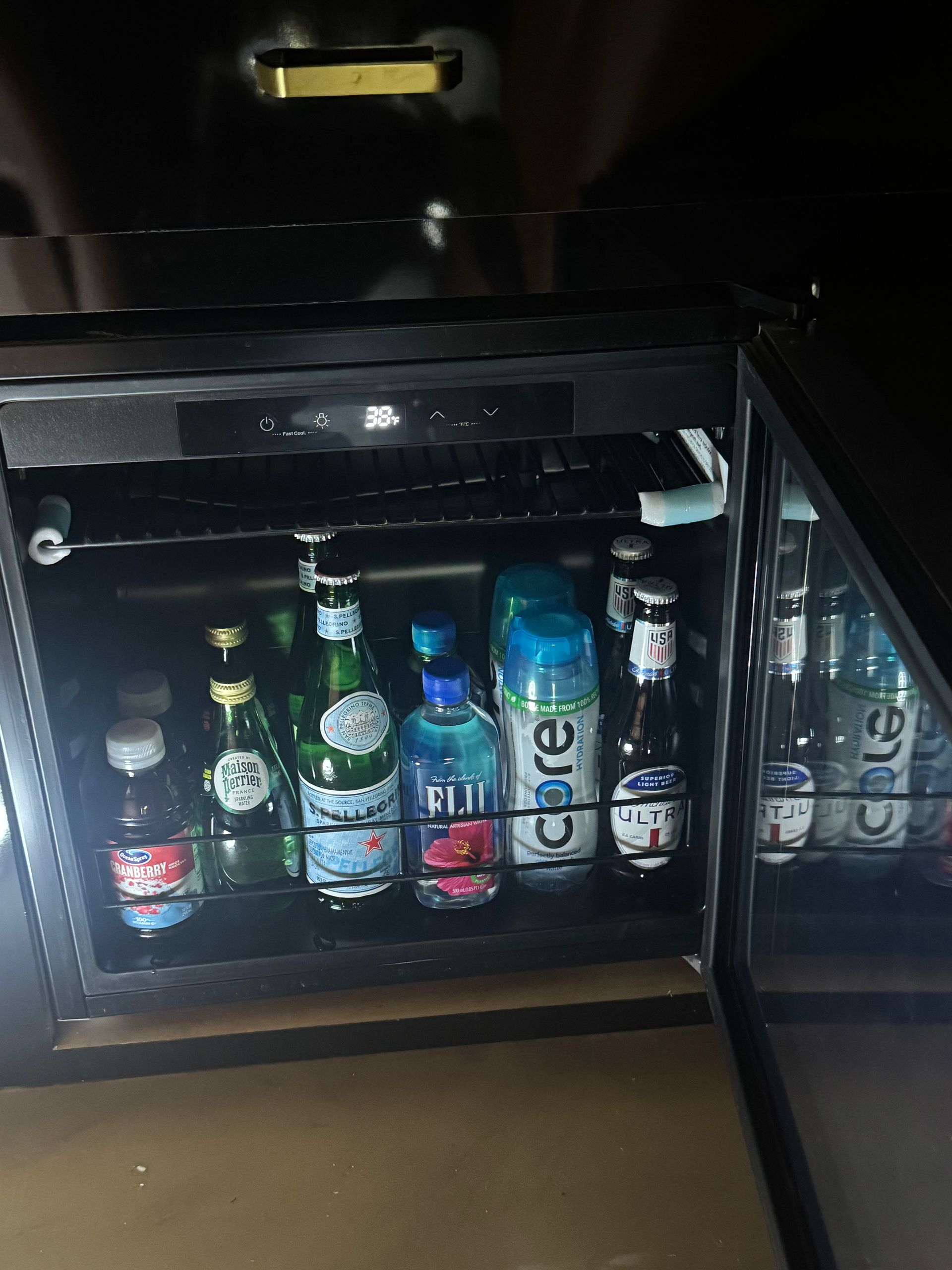 Mini fridge stocked with assorted drinks, including bottles, cans, and a tall blue can.