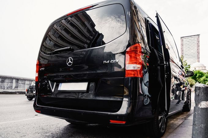 Black Mercedes van parked on a wet street, rear view with city buildings in the background