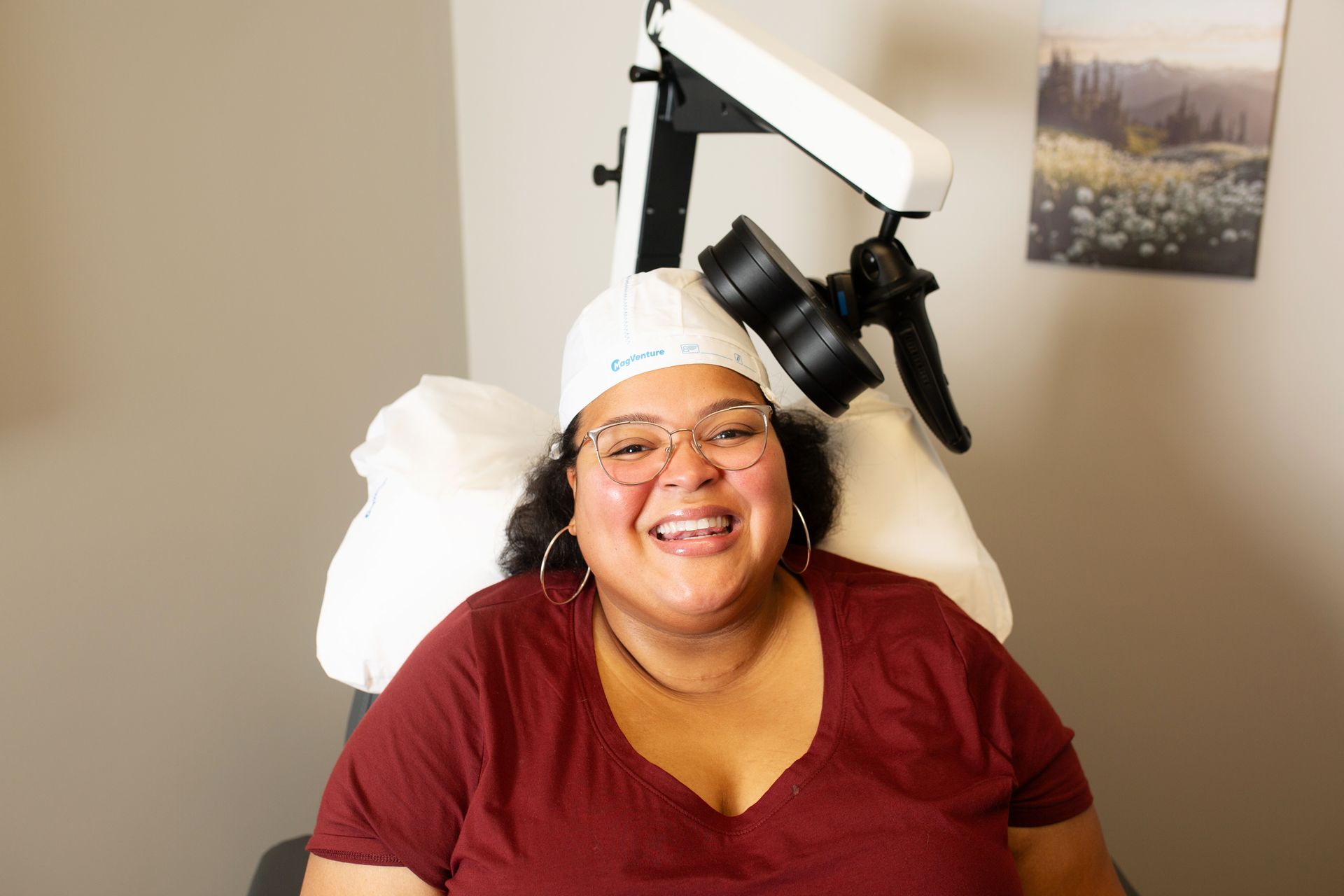 Woman smiling, wearing a hat, sitting in a medical chair, next to a machine.