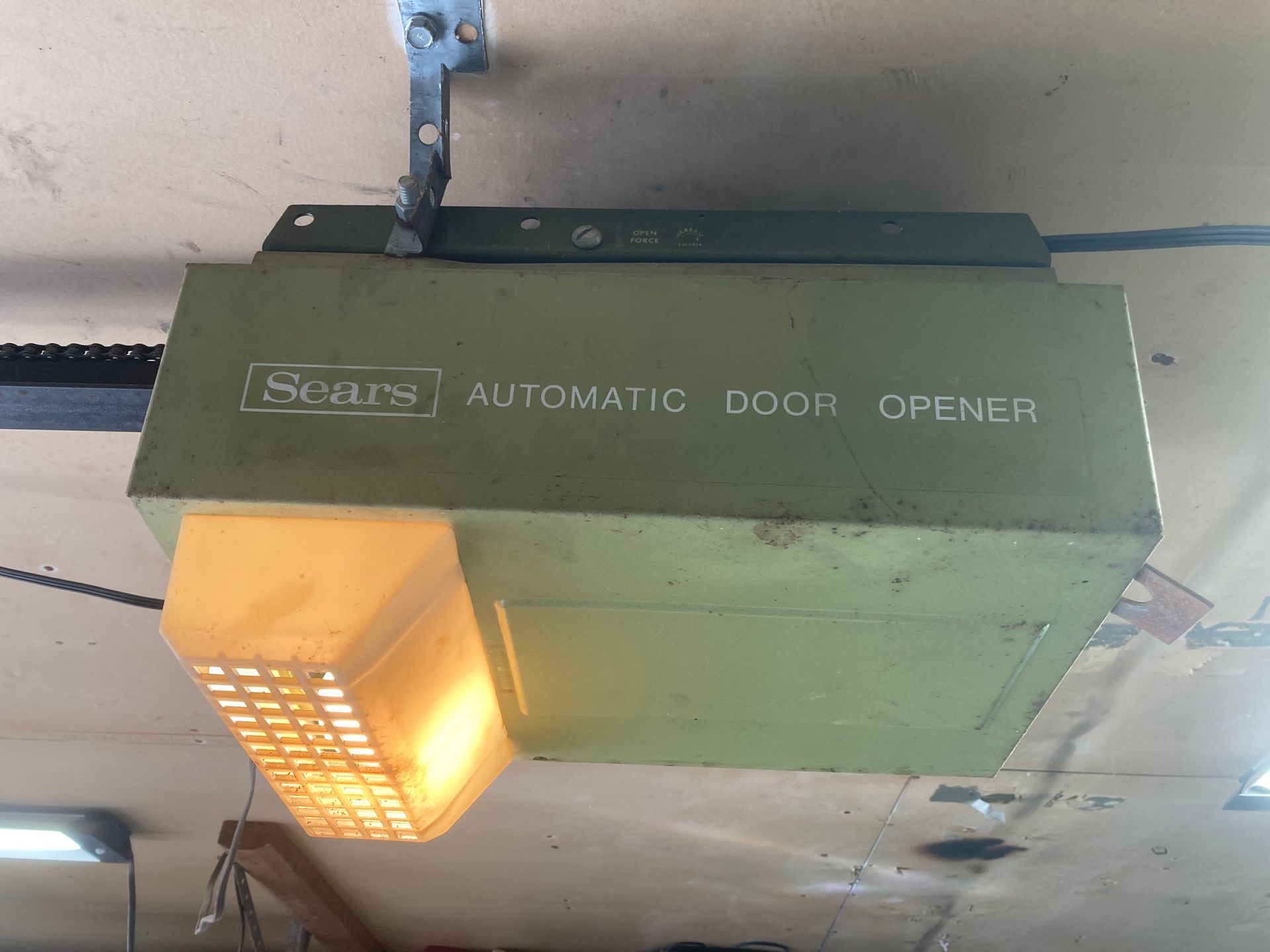 Green garage door opener with a lit orange bulb mounted on a ceiling.