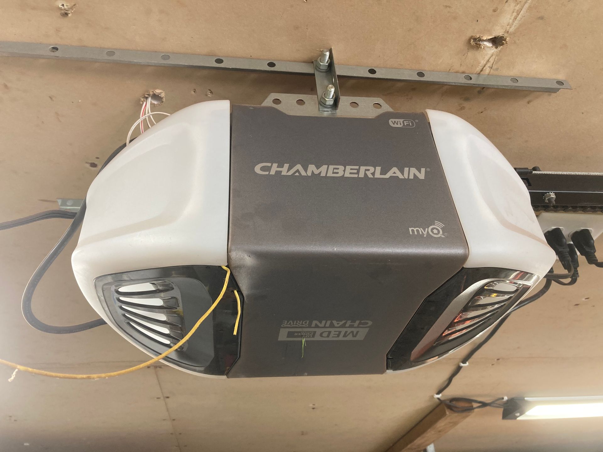 White Chamberlain garage door opener mounted on a ceiling, with black side vents and yellow wires.
