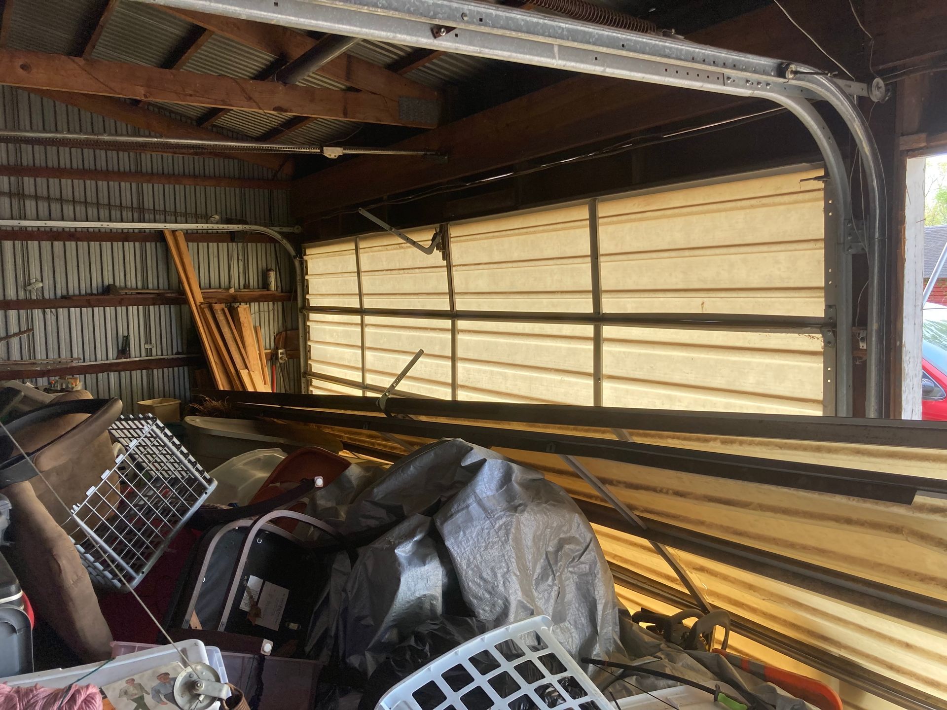 Inside a cluttered garage, tools and materials are piled beneath a partially open door.