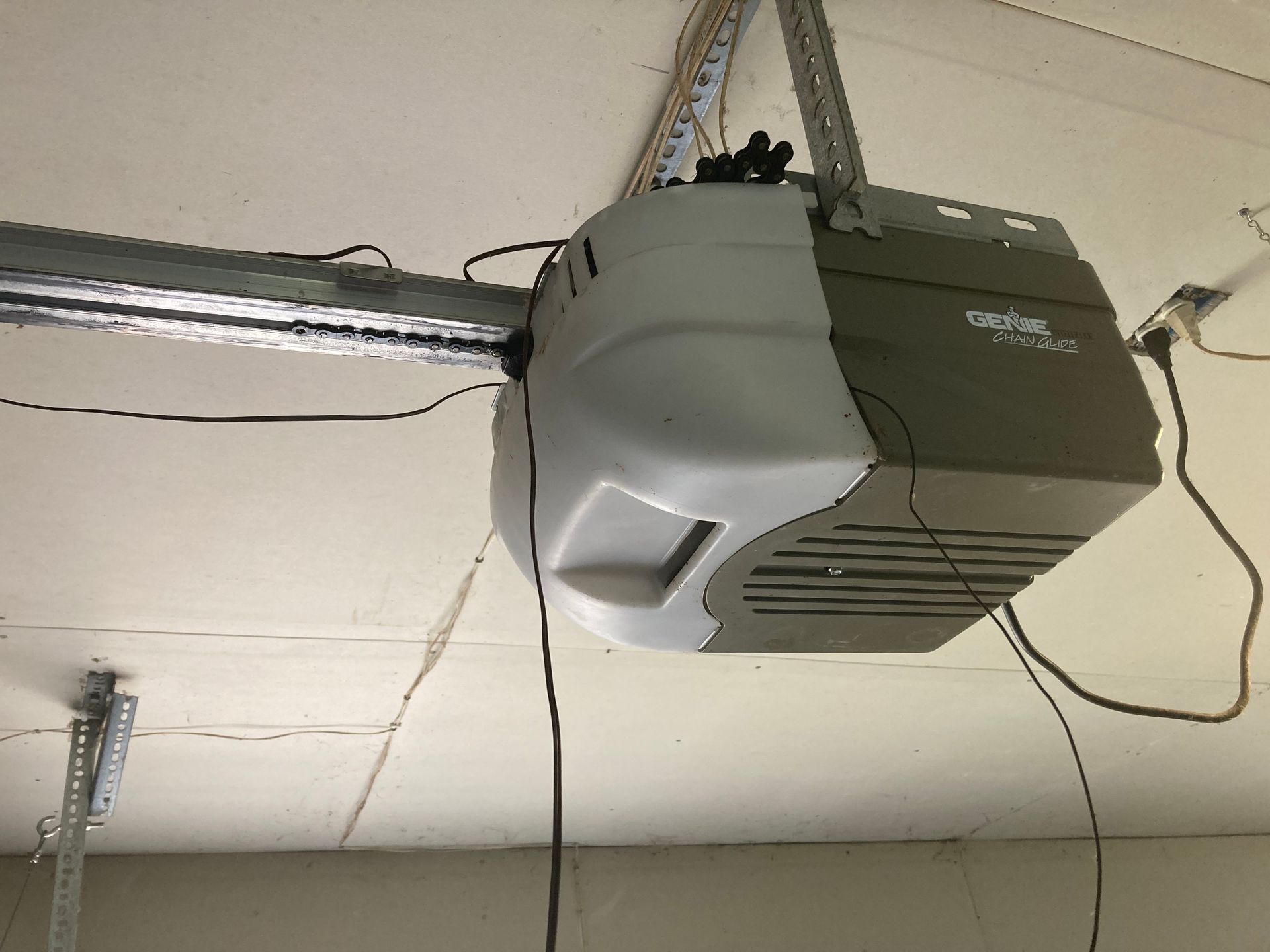 Ceiling-mounted gray garage door opener with rail and hanging cables.