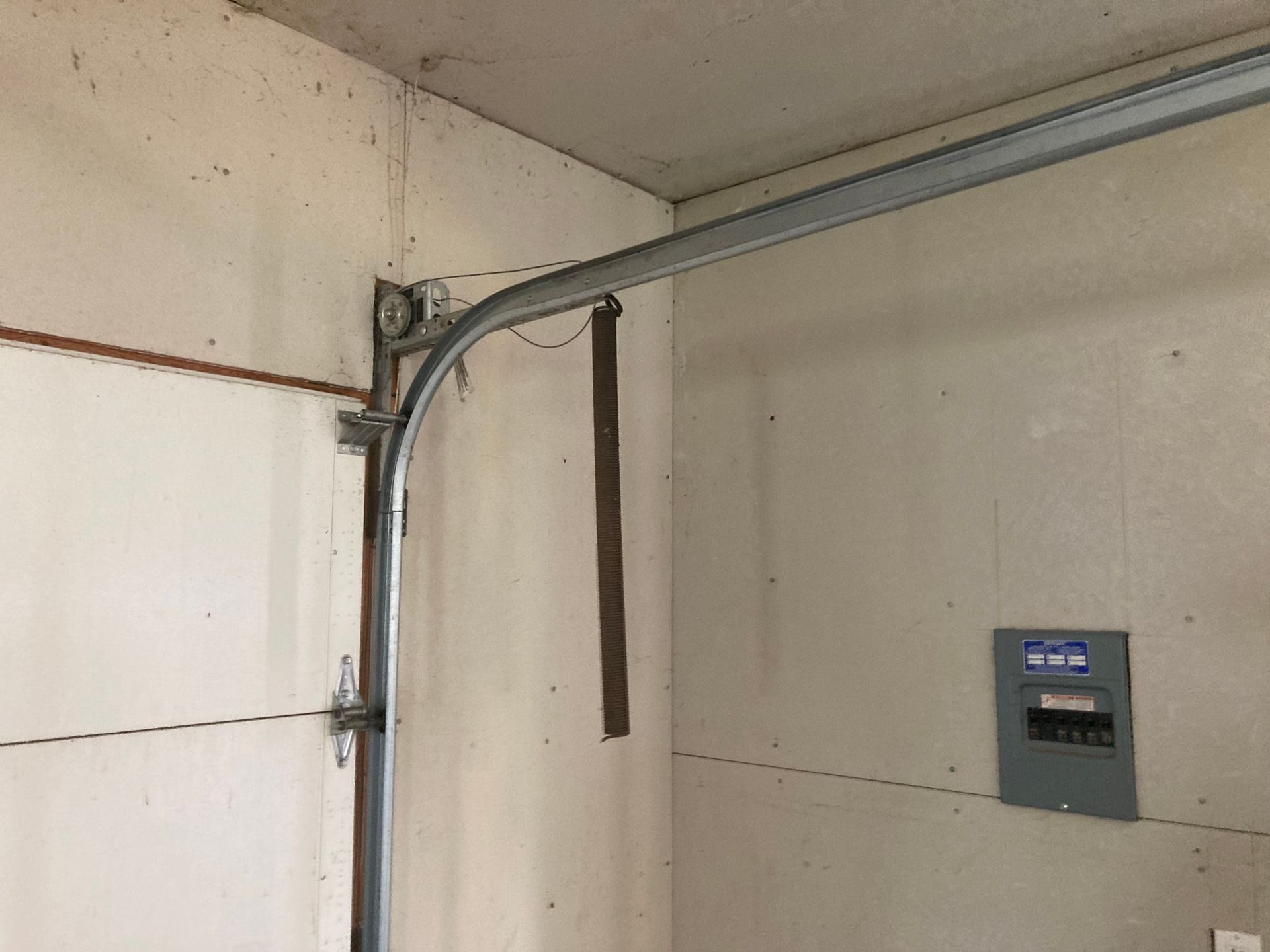 Garage wall with a metal door track and opener, plus a small wall-mounted control panel.