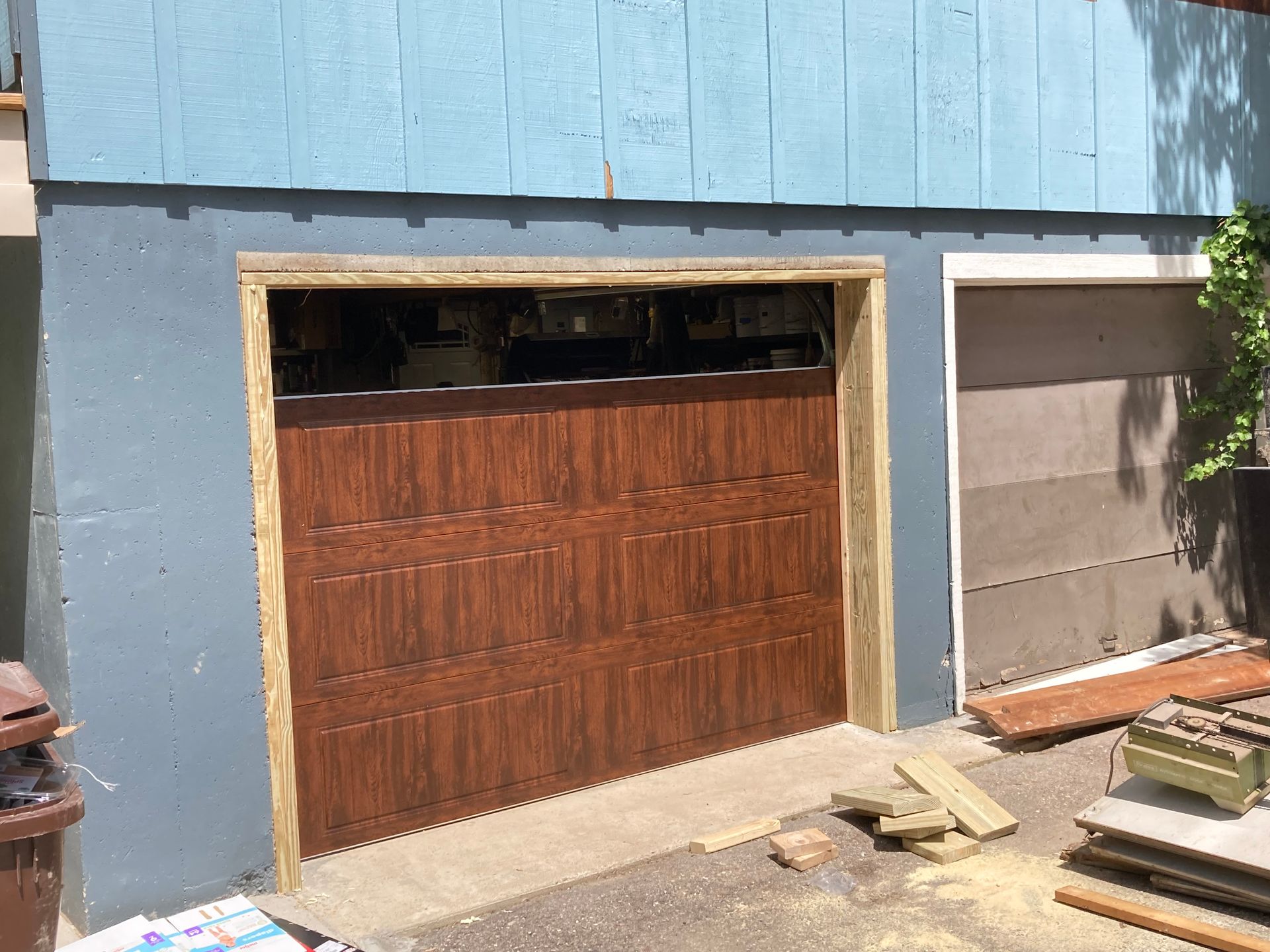 Blue house exterior with a wooden garage door and construction materials nearby