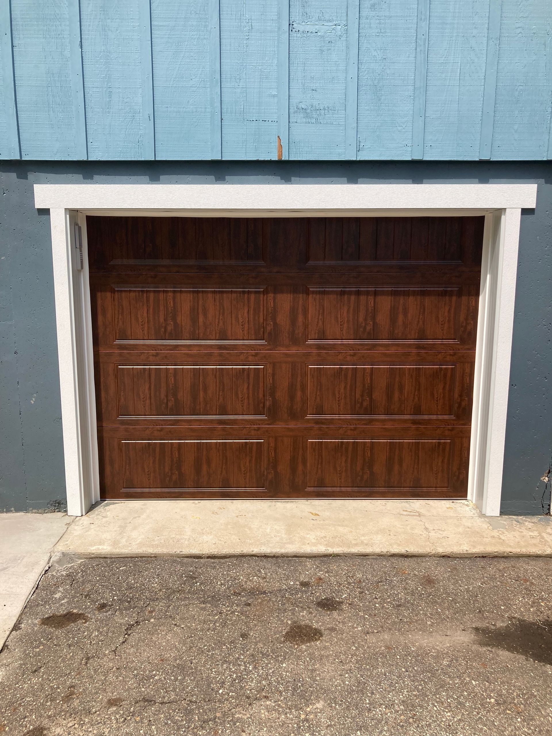 Wooden garage door set in a blue building wall with white trim and concrete driveway.