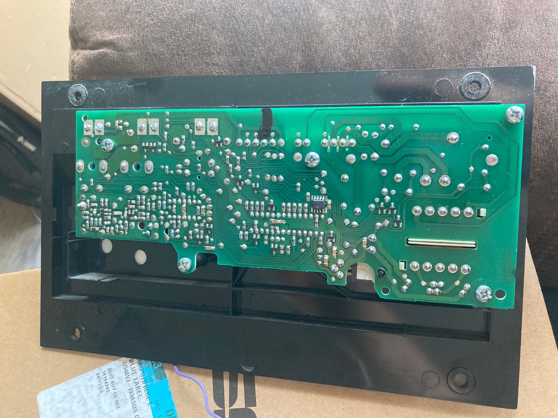 Green circuit board mounted on a black plastic housing, viewed from the back against a cardboard surface