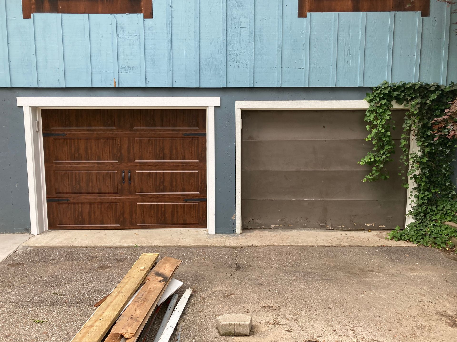 Two garage doors on a blue building with wood planks and a small pile of boards in front