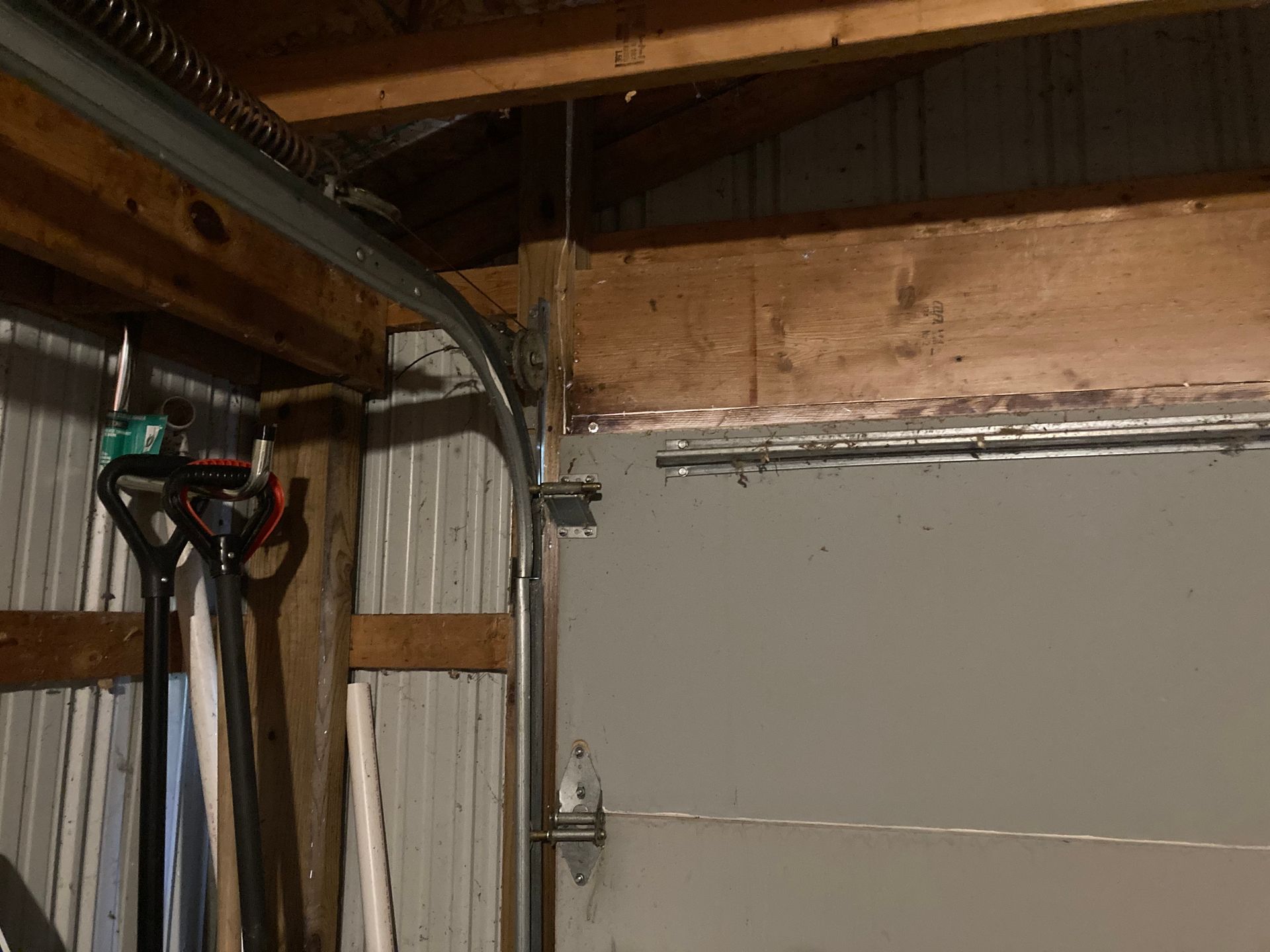 Garage interior with a closed gray door, exposed beams, and hanging tools on the left