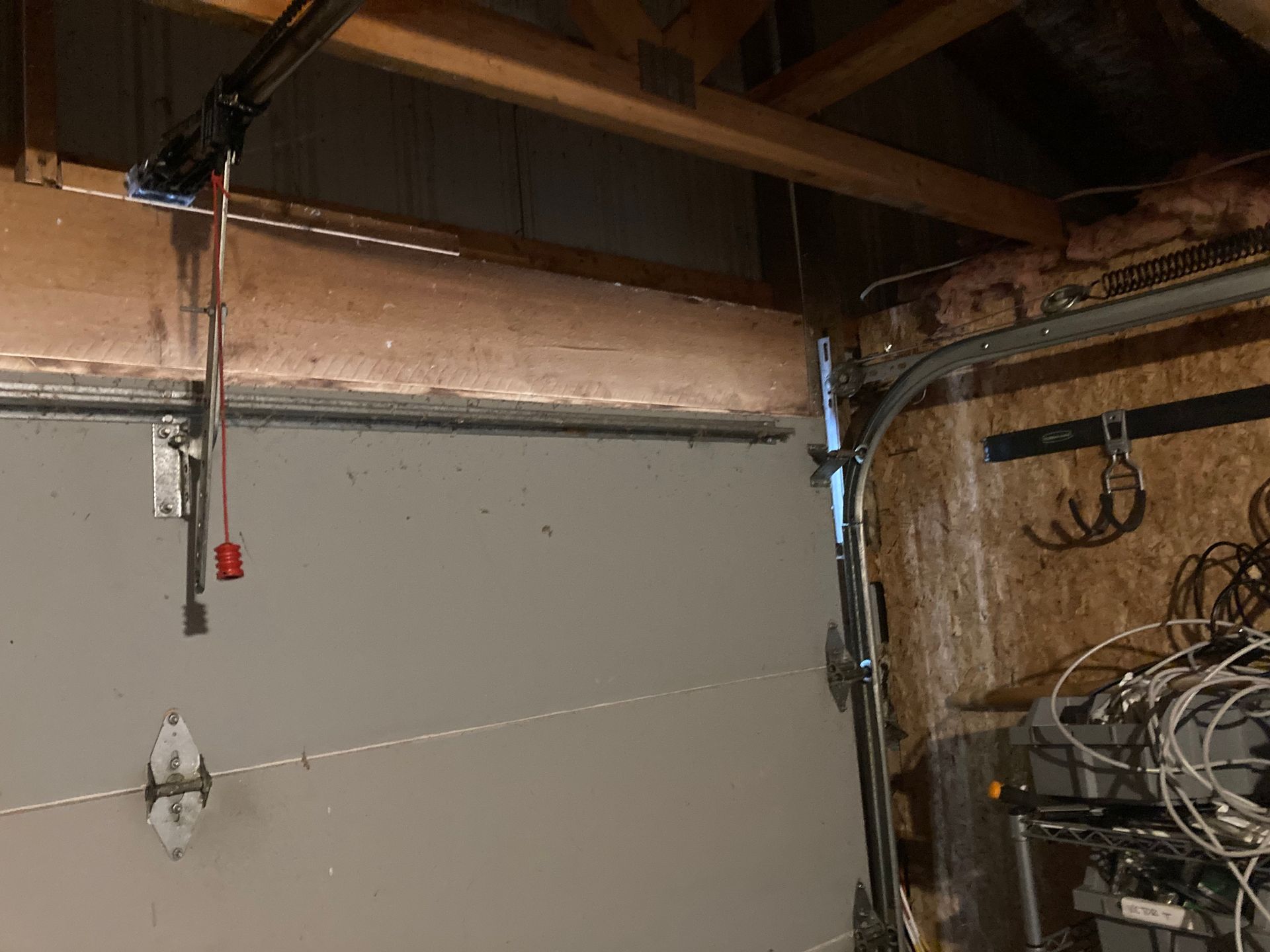 Garage interior with a gray door, exposed beams, and storage items on the right
