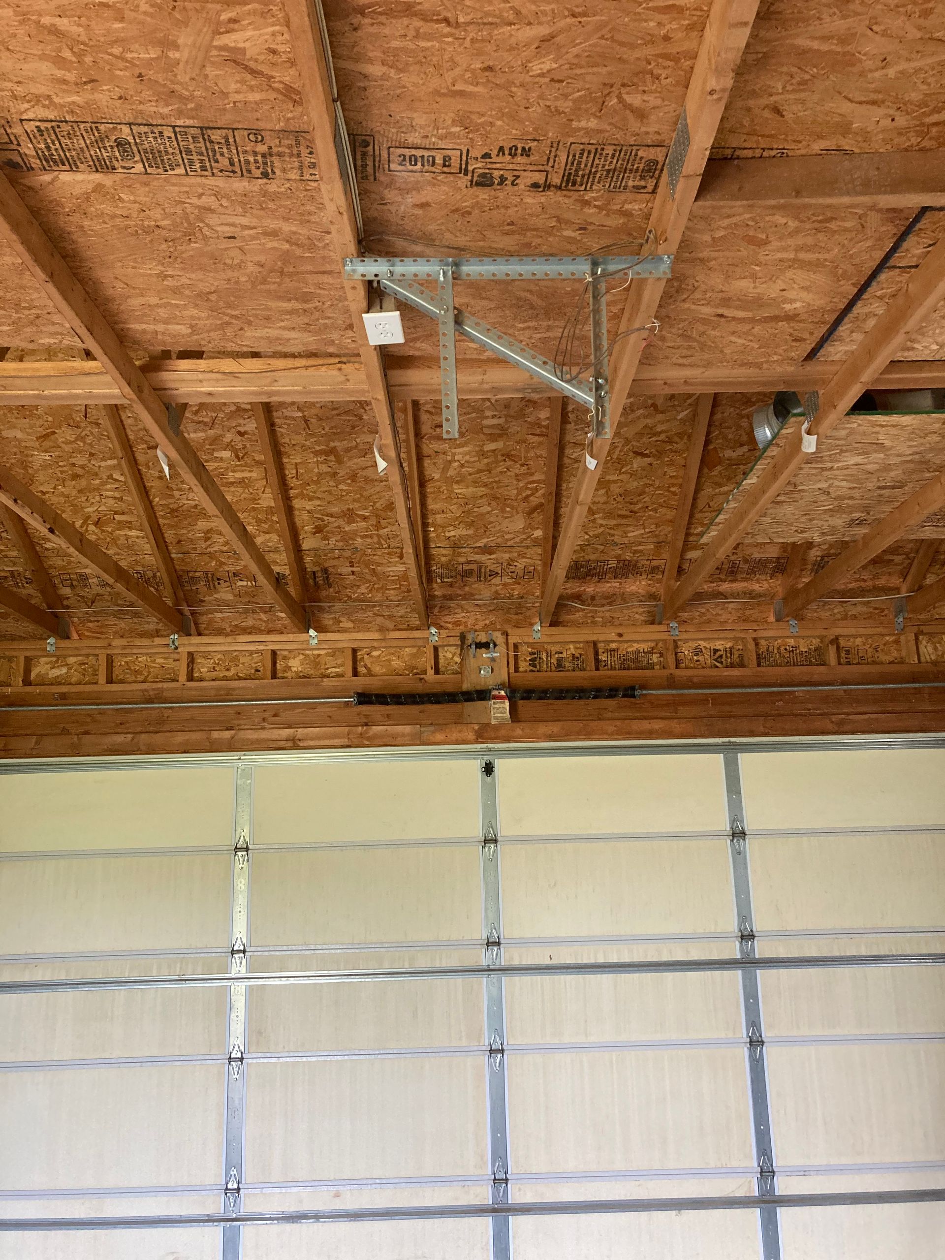 Exposed wooden ceiling with metal bracket and unfinished garage wall panels beneath