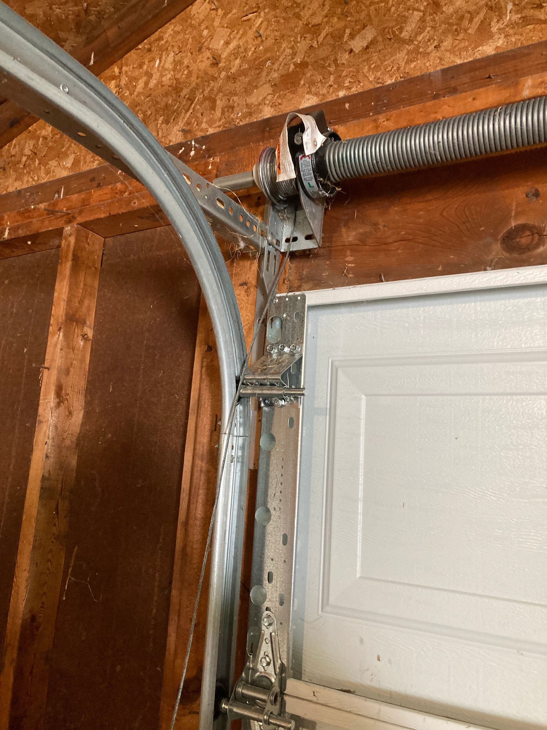 Garage door opener track and spring mounted beside a white garage door.