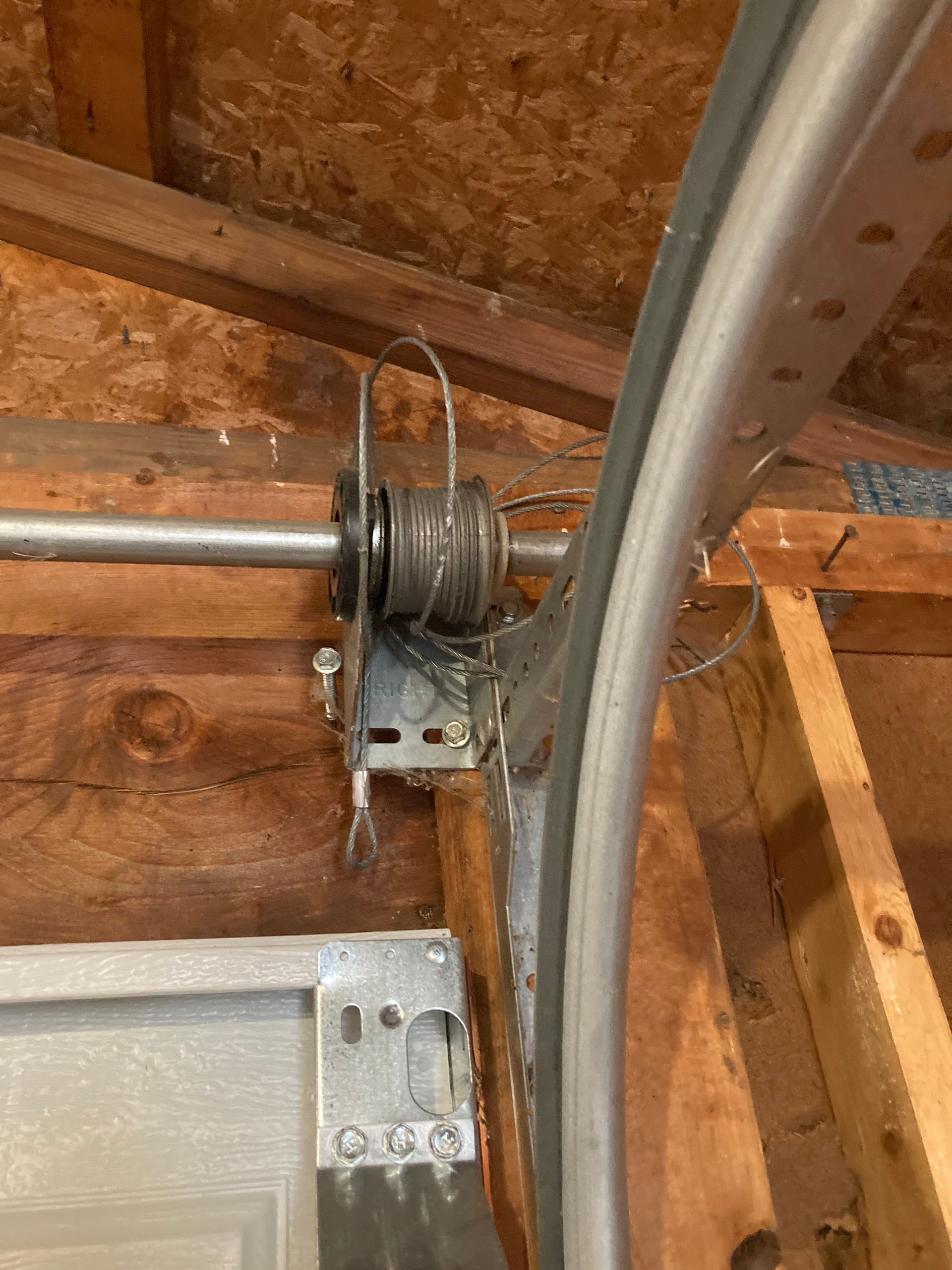 Garage door spring mechanism mounted to a wooden ceiling near the door track.