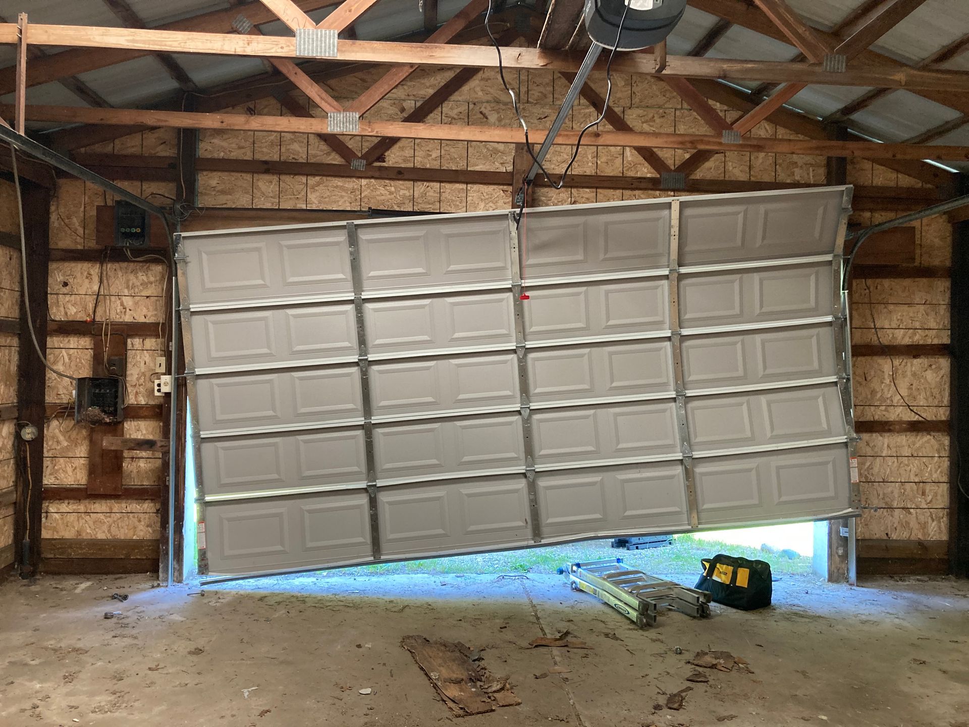 Partially open white garage door inside a wooden-framed garage, with blue daylight visible underneath