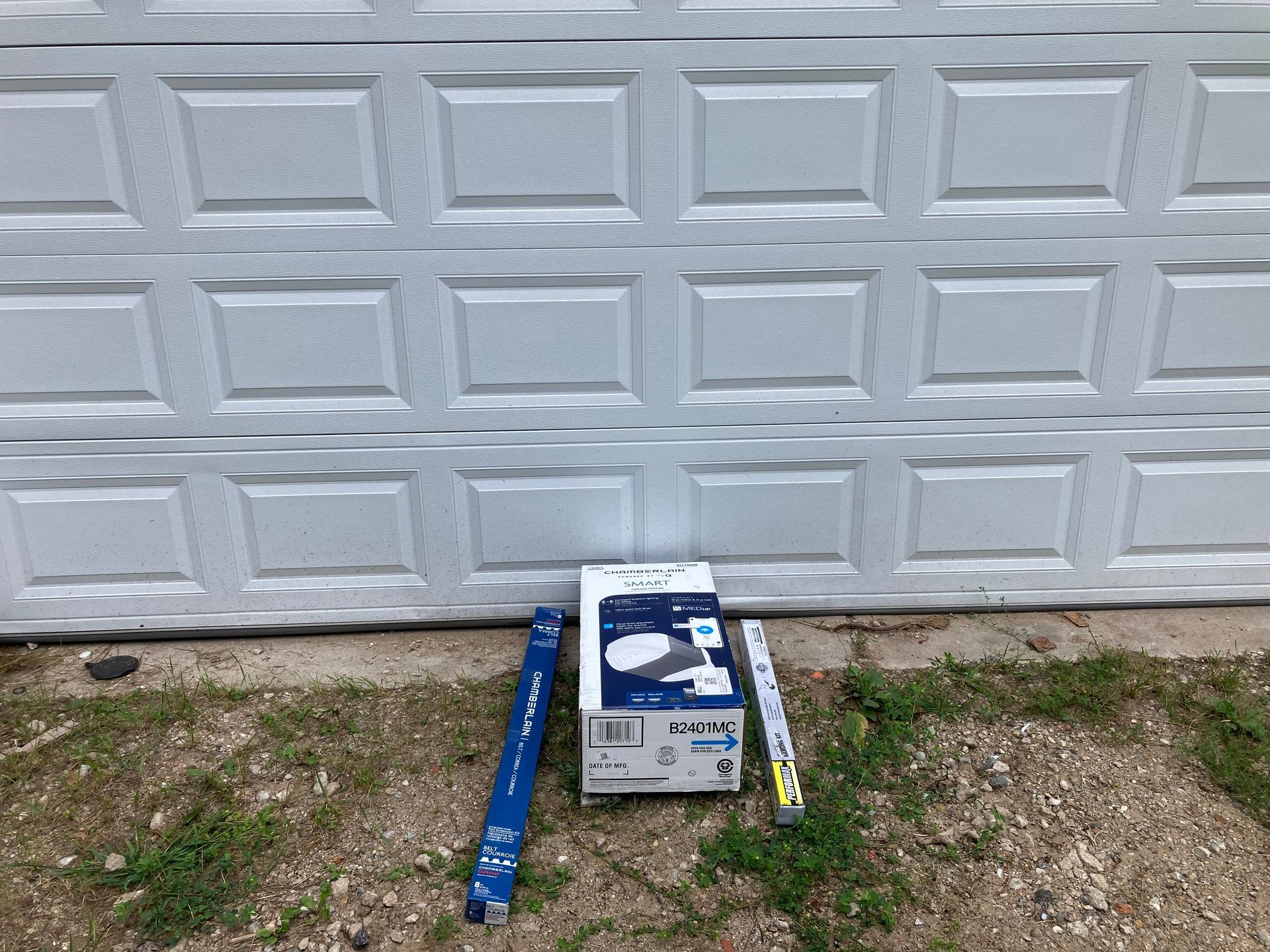 Box and long blue objects on gravel in front of a white garage door.