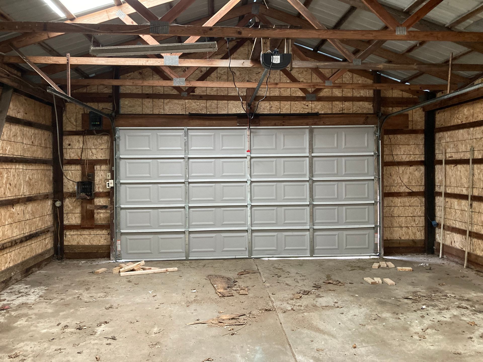 Empty garage interior with closed gray overhead door and exposed wooden beams