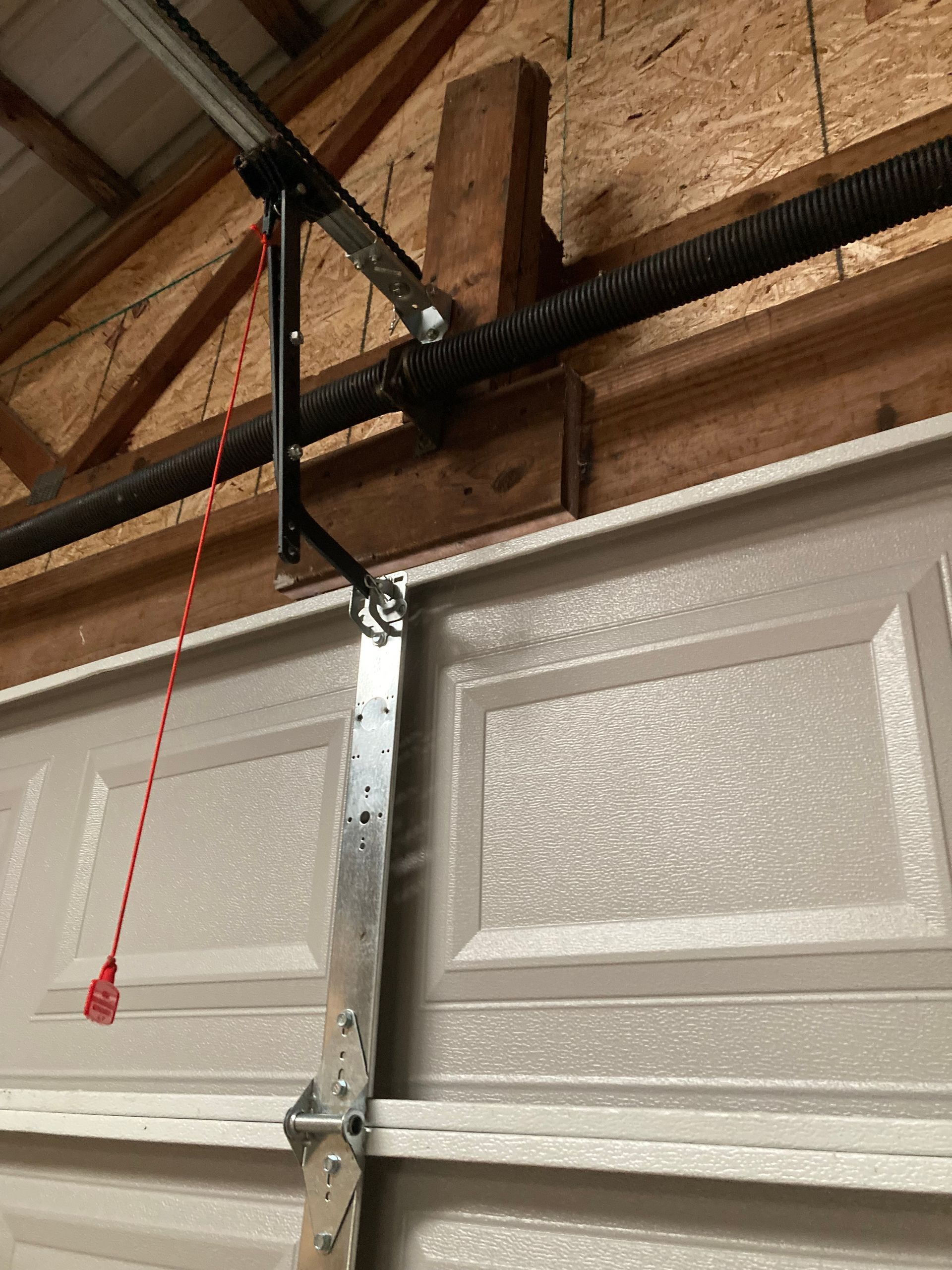 Garage door opener with metal support bracket mounted to a white overhead garage door.
