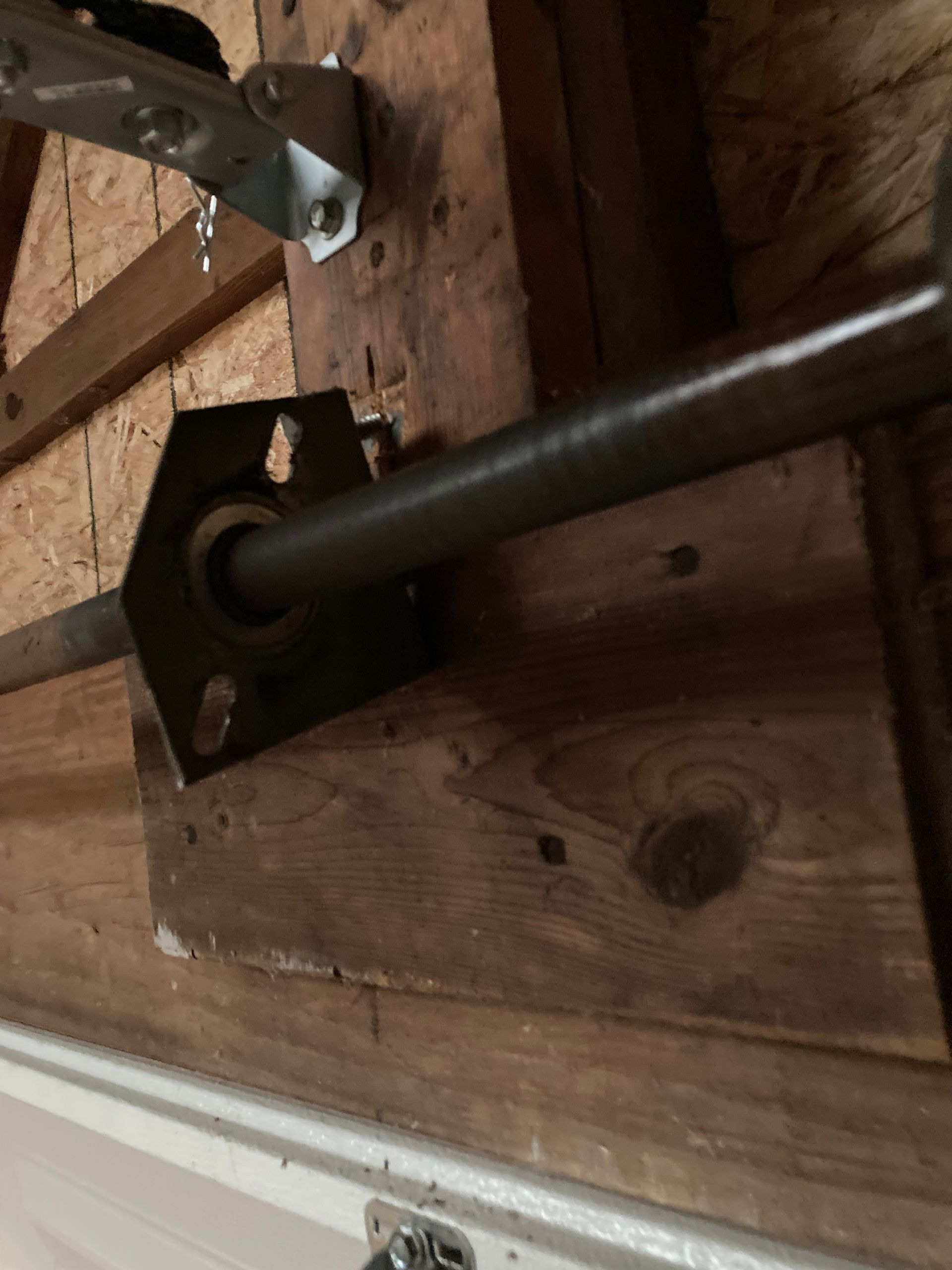 Metal pipe bracket mounted to wooden beams in an unfinished attic or crawl space.