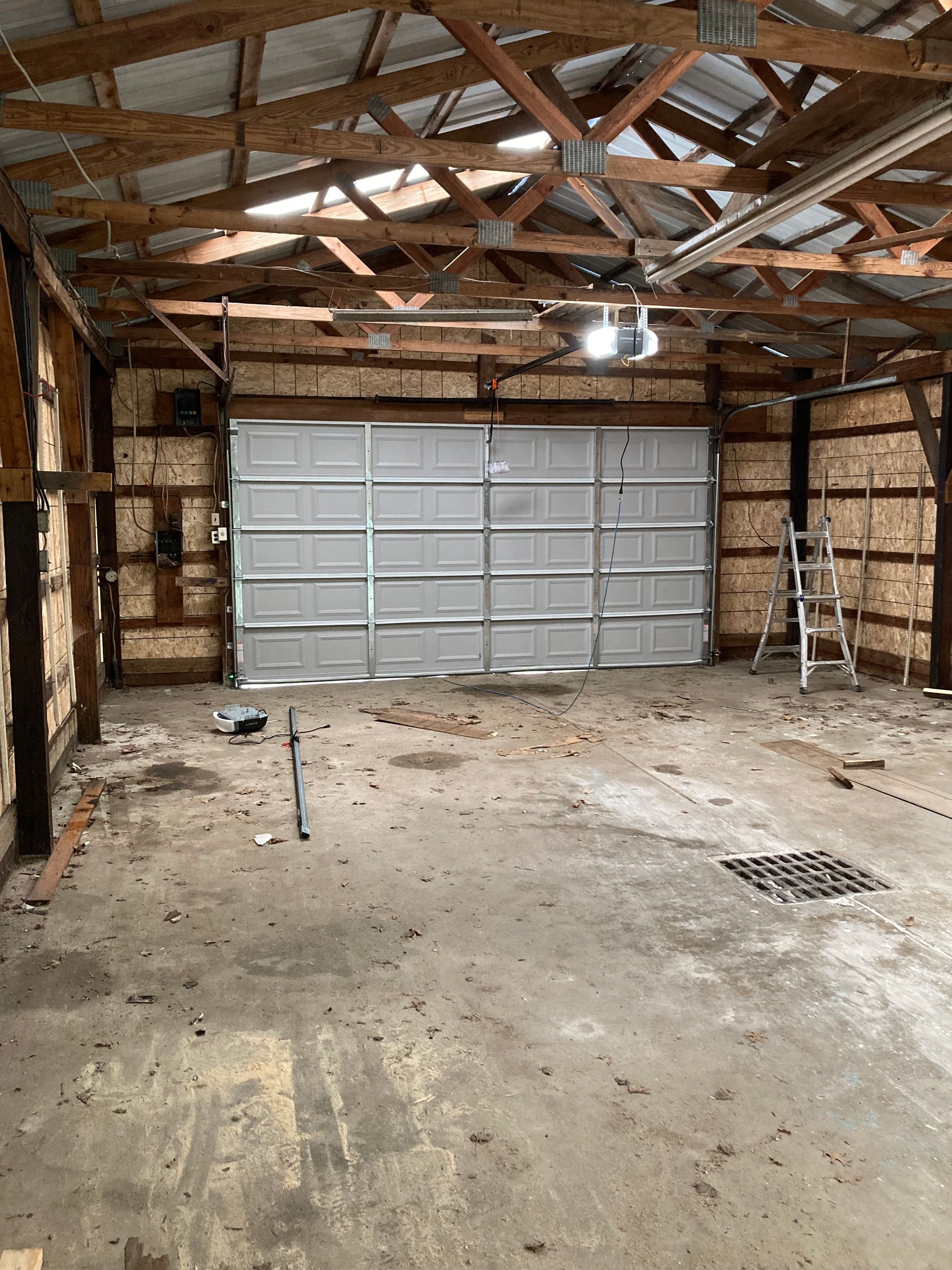Empty garage interior with exposed rafters, concrete floor, and a closed gray metal door at the back.