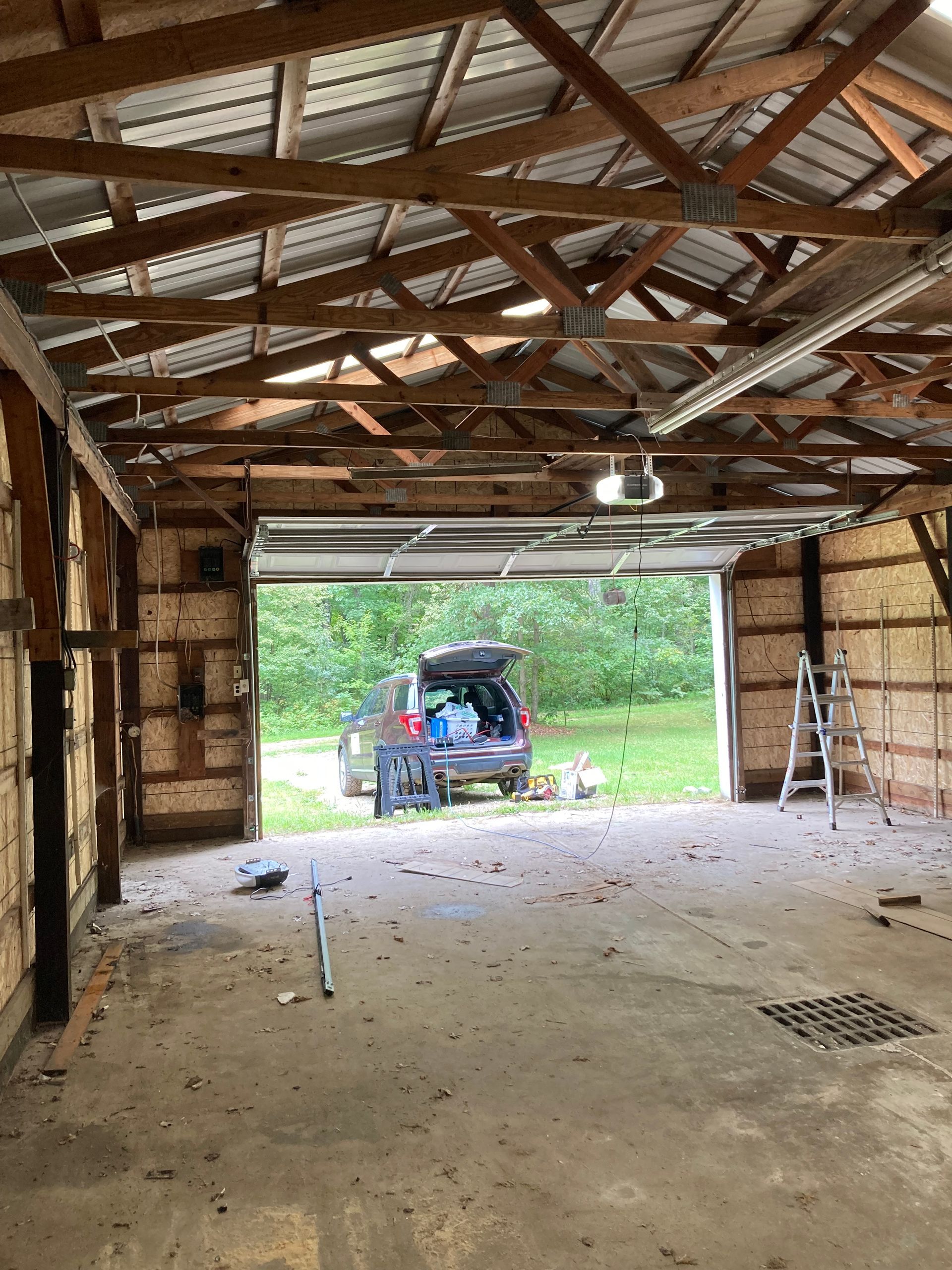 Interior of a rustic garage with a car parked in the open doorway and a ladder on the right.