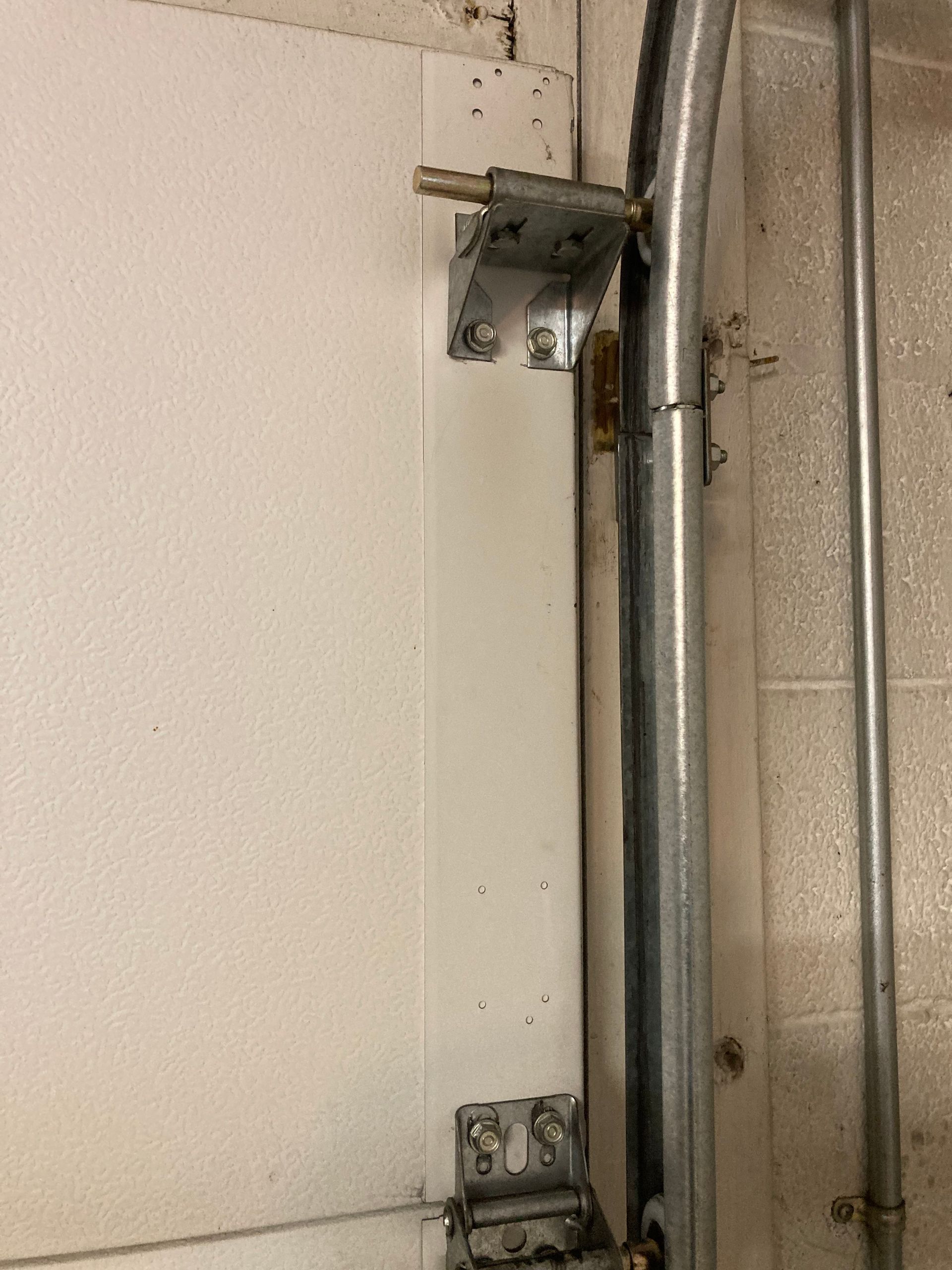 Garage door track and metal hardware mounted beside a white wall.