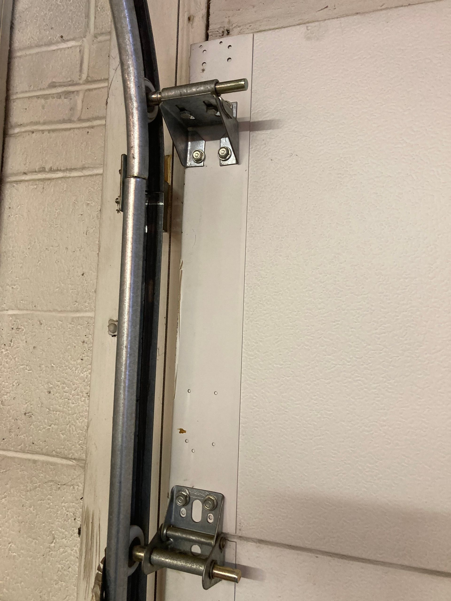 Wall-mounted metal brackets and a black conduit beside a white panel on a cinderblock wall