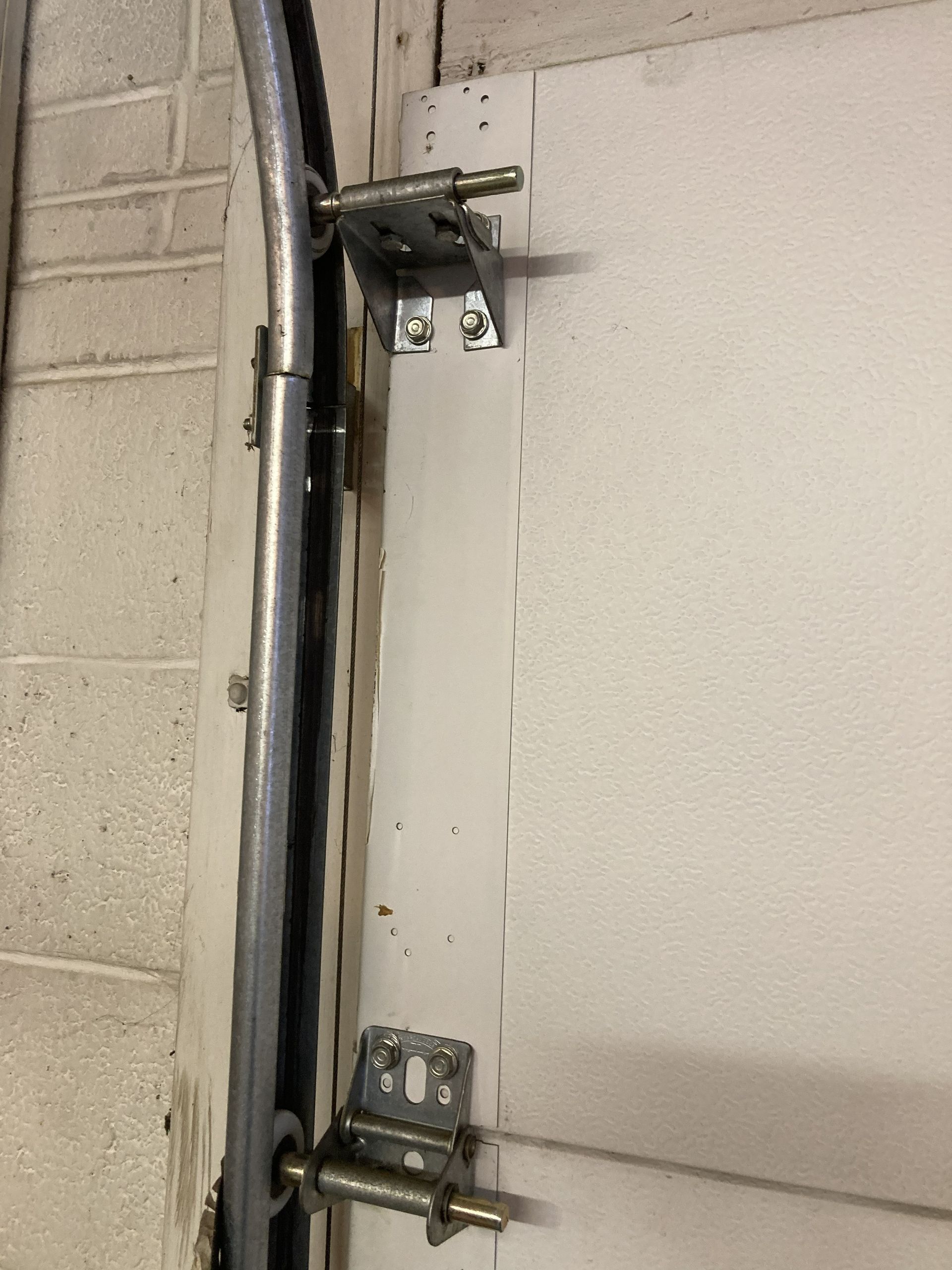 Metal door hinges and latch mounted on a beige wall, viewed close-up.