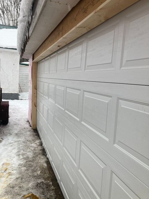 Snow-covered driveway beside a white garage door under an overhang