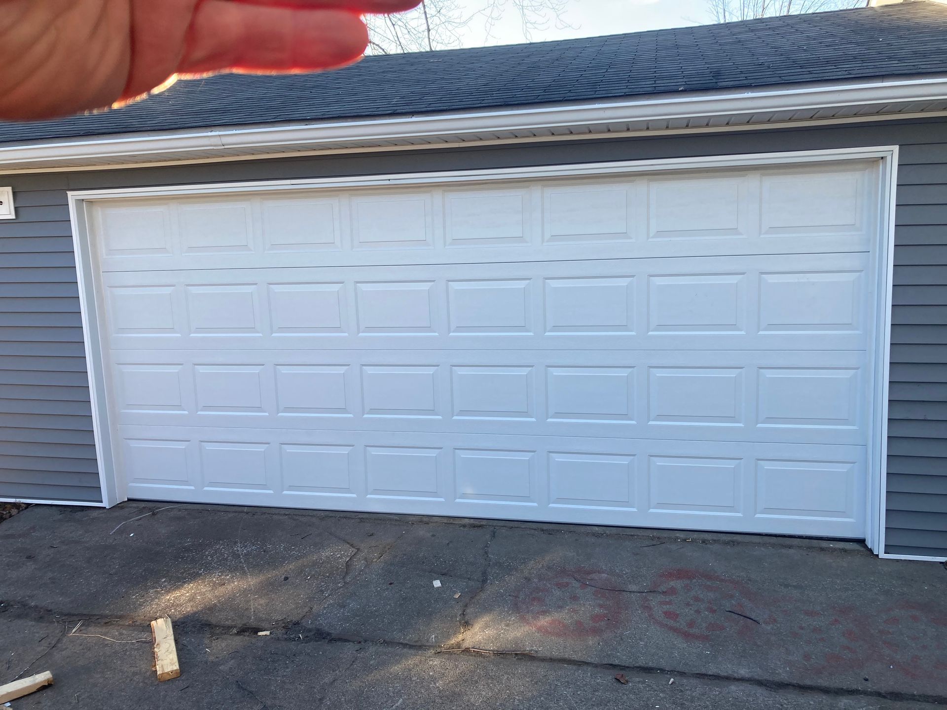 White double garage door with rectangular panels, seen on a driveway beside light gray siding.