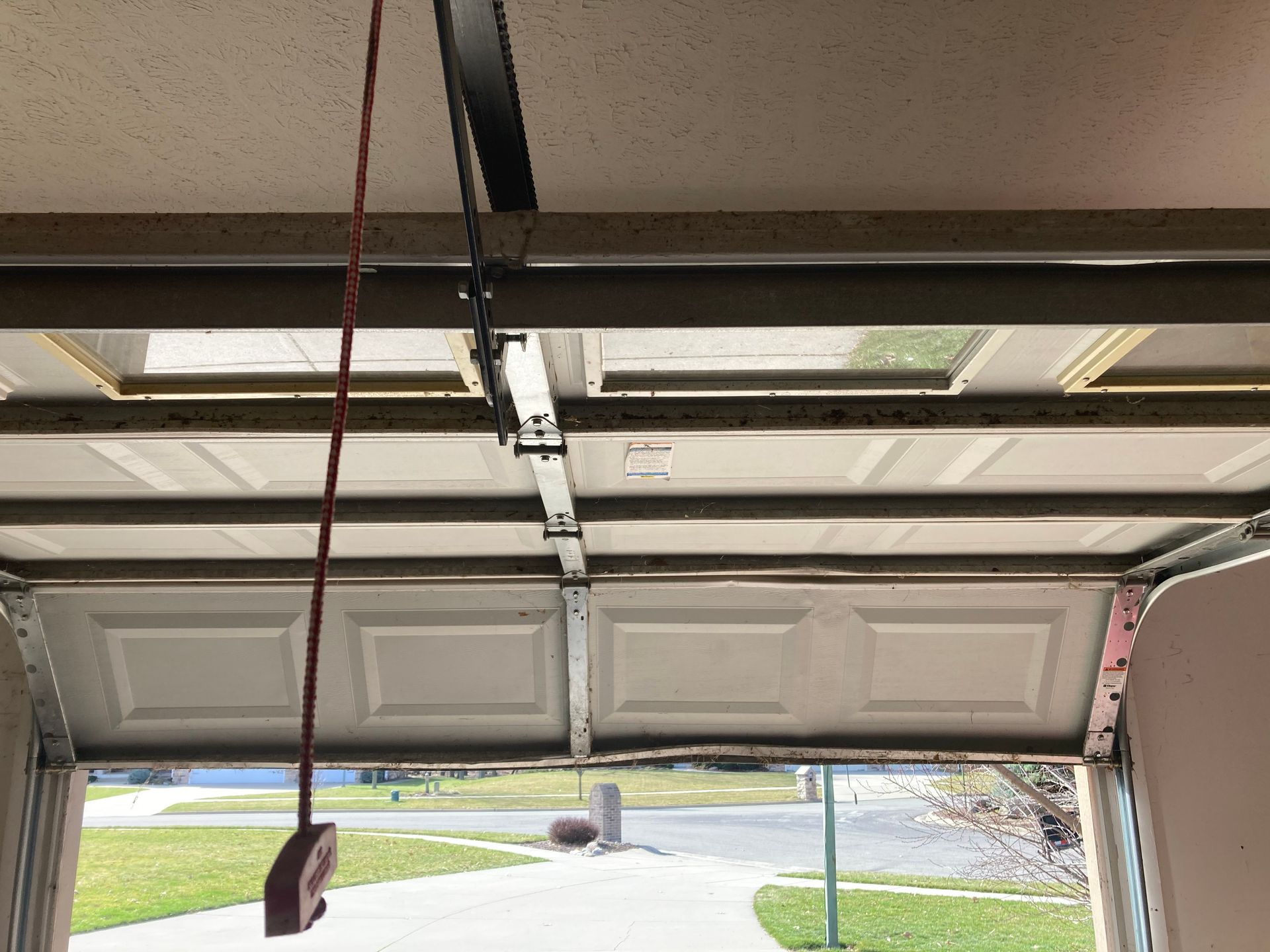 Open garage door showing the underside of the door panels and opener track, with daylight outside.