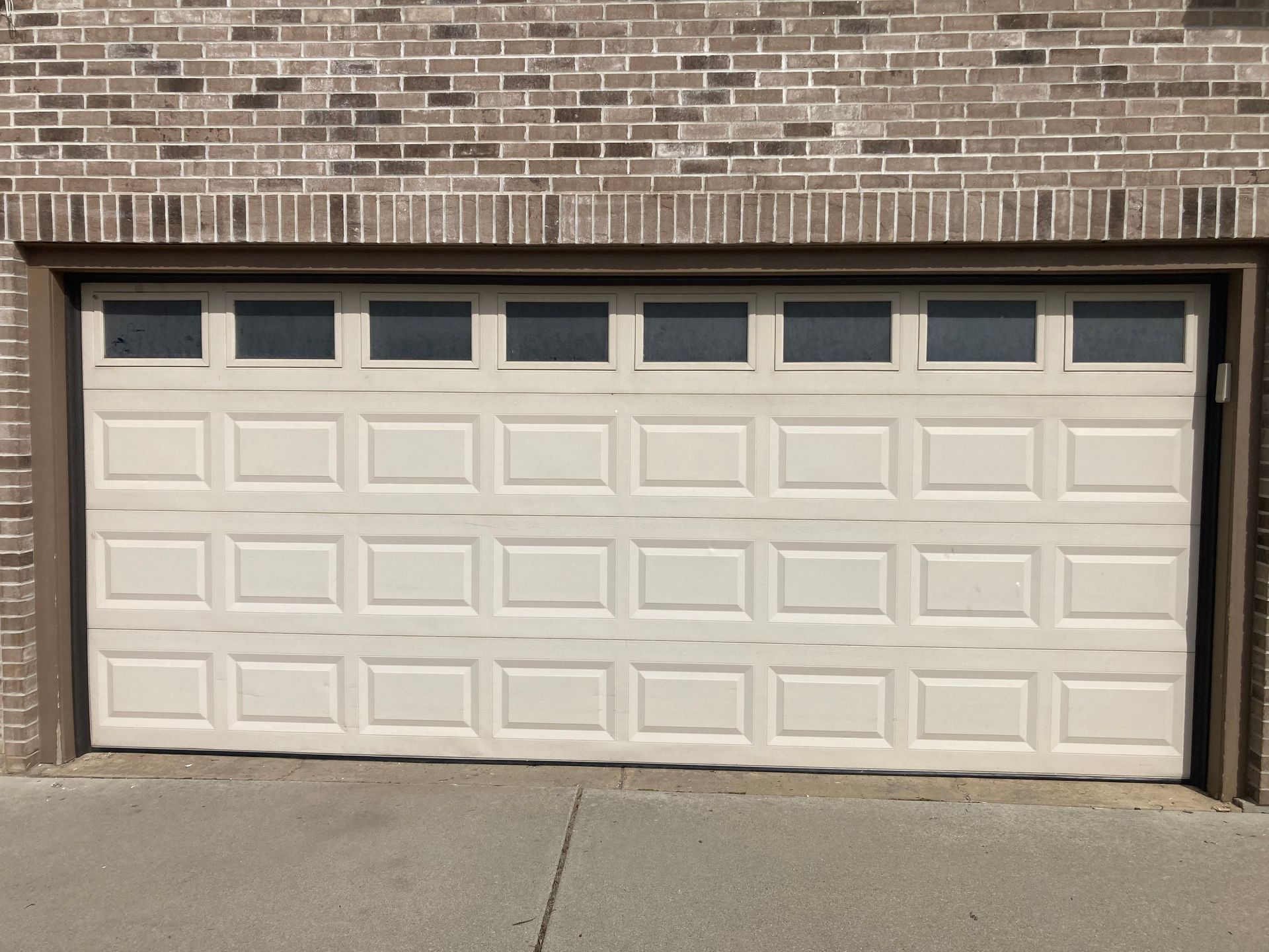 White double garage door with small windows set in a brick house facade.