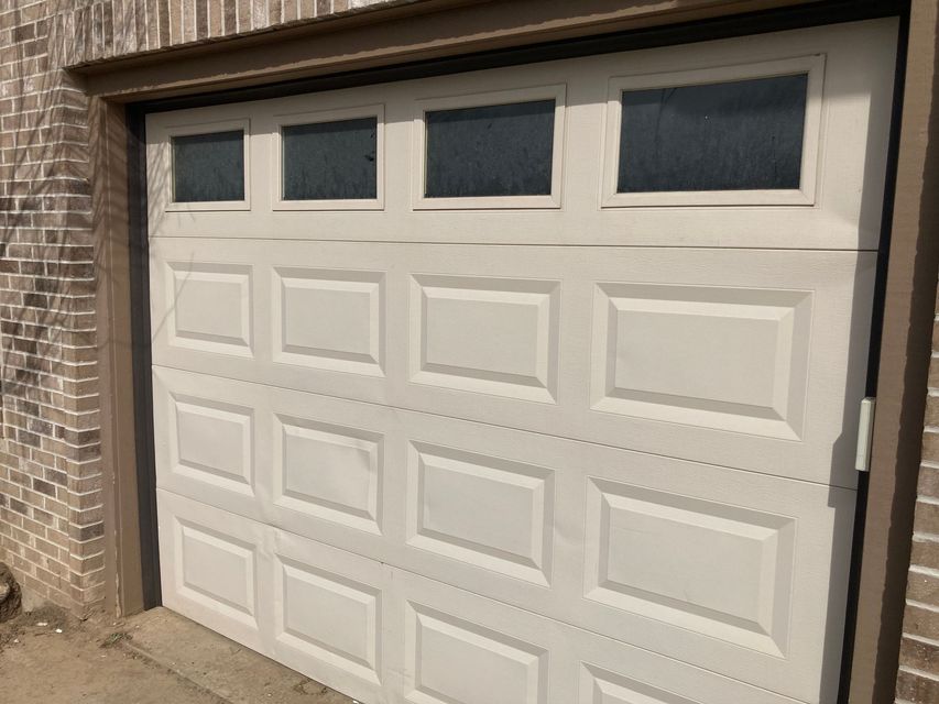 White paneled garage door with four small windows at the top, set in a brick exterior