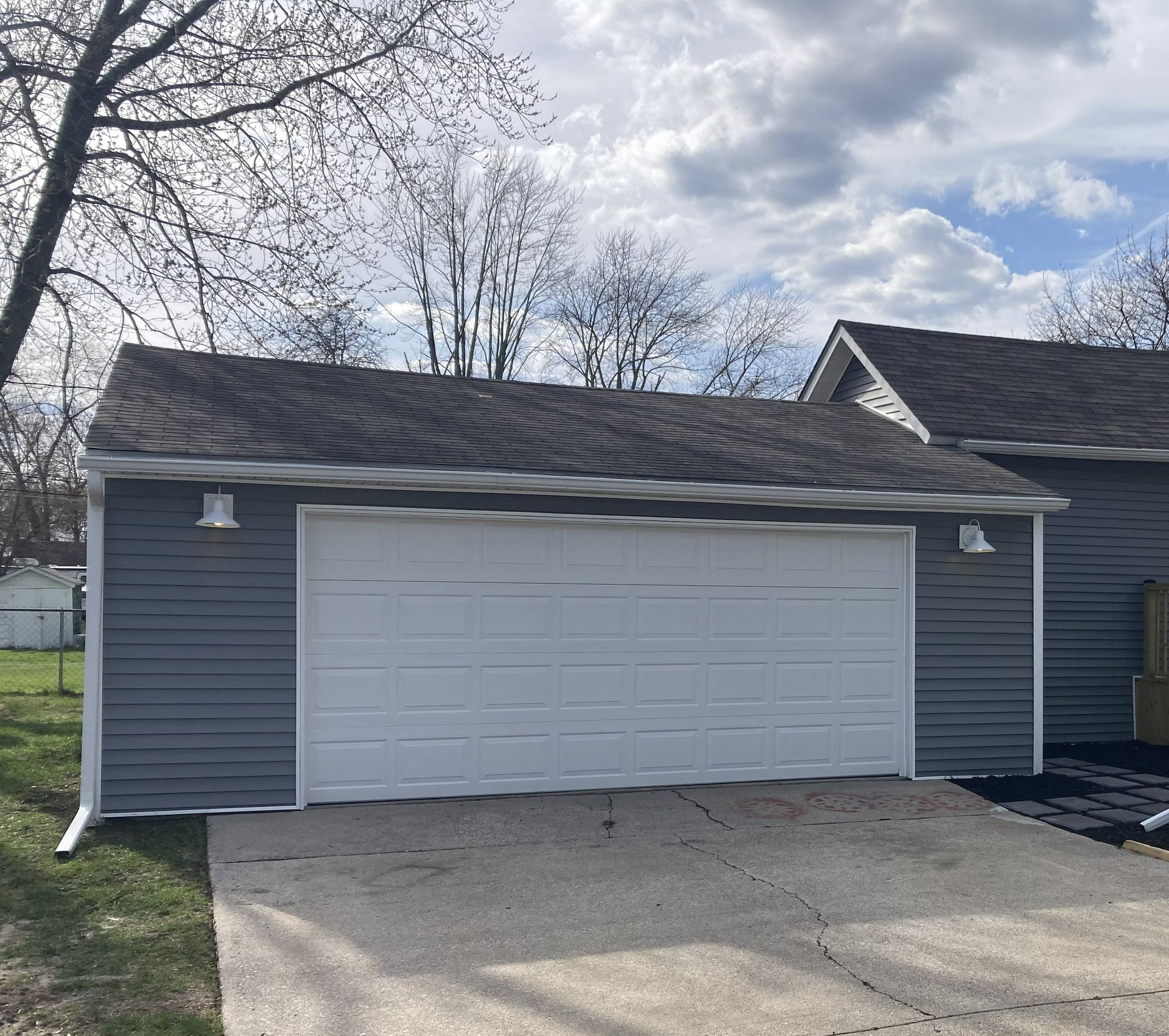 Blue detached garage with white doors and a sloped driveway under a partly cloudy sky